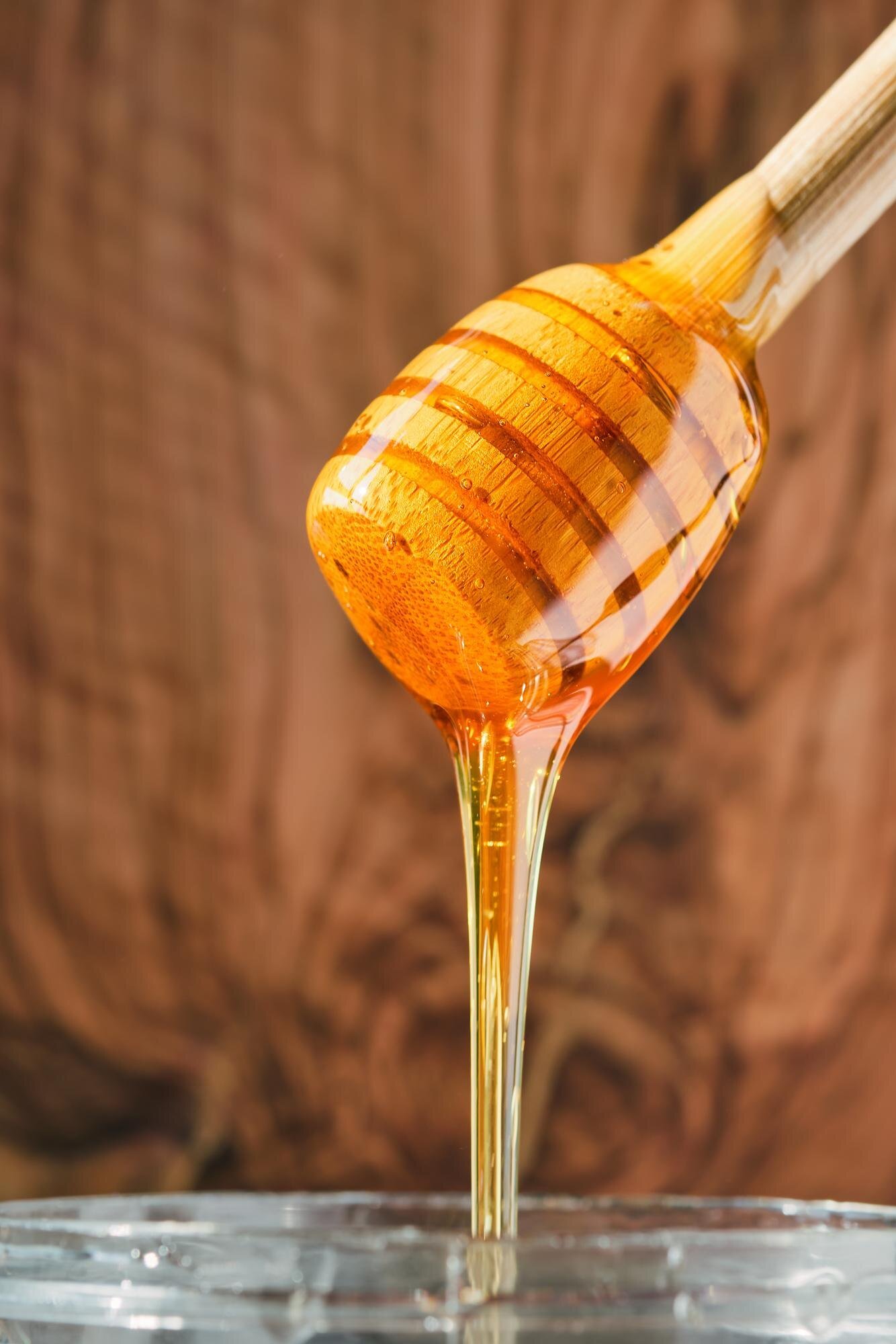 honey-flows-from-wooden-honey-stick-into-jar-vertical-shot-closeup-selective-focus-honey-natural-slab-background-natural-products-from-farms-turkey_166373-3548